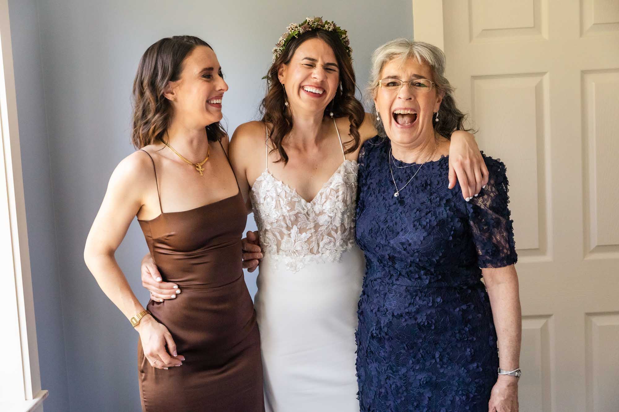 mother of the bride, bride, and her sister laugh together in a relaxed candid feeling portrait. these are the types of portraits to expect when you hire a photojournalist who photographs weddings